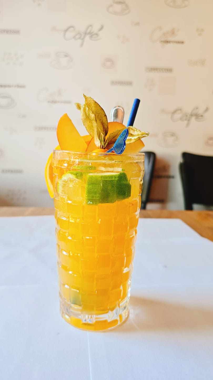 Ein Glas mit gelbem Getränk, Limette, Physalis und Strohhalm auf einem Tisch in einem Café.